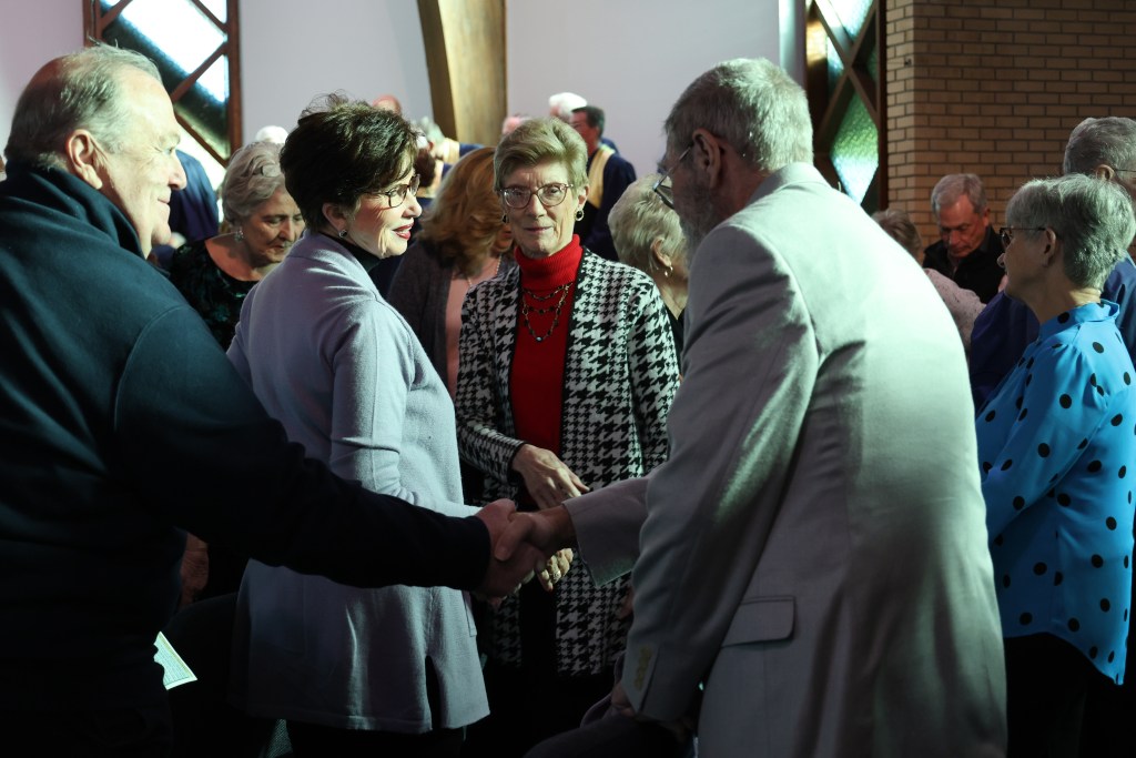 Group of older adults greeting one another and shaking hands during a church or community gathering.