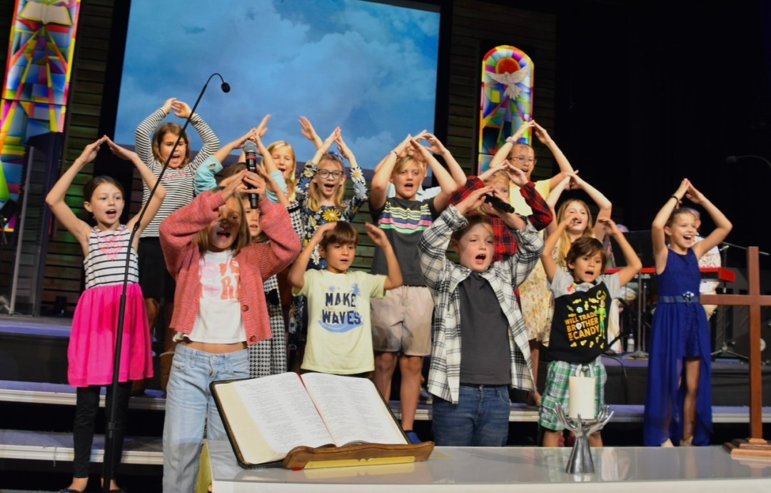 Children’s choir performing on church stage with open Bible and worship elements in foreground